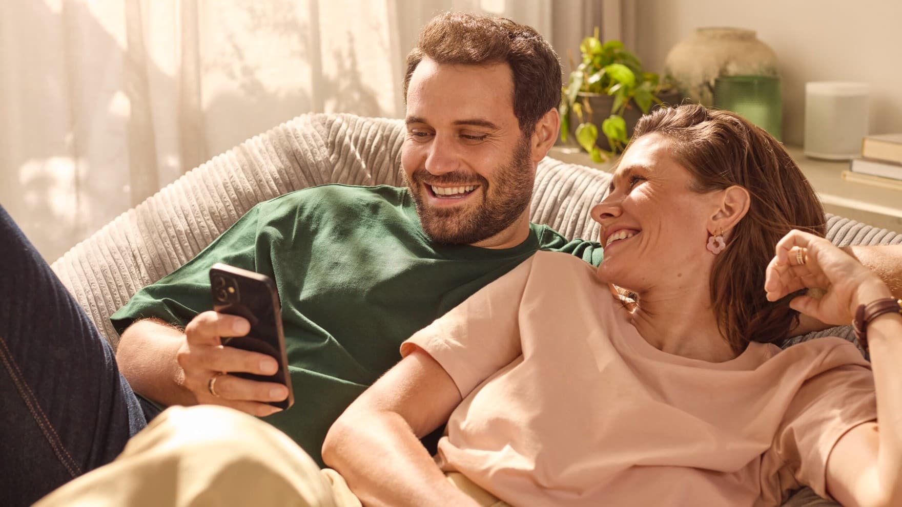 Pár sedící na gauči a dívající se na telefon