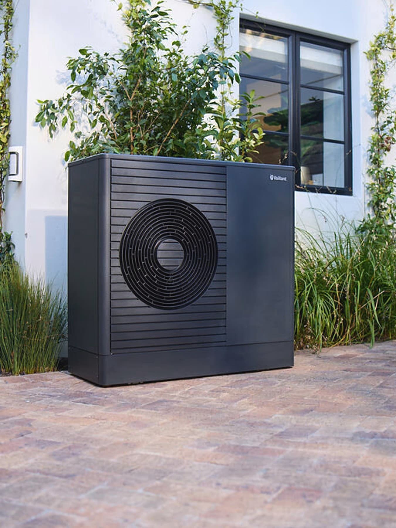 Tmavé tepelné čerpadlo Vaillant aroTHERM plus v předzahrádce domu