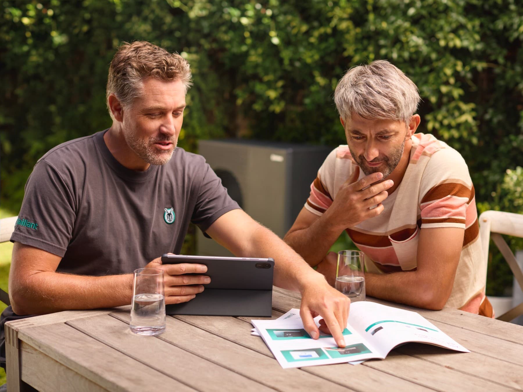 Dva muži před tepelným čerpadlem s prospektem na stole