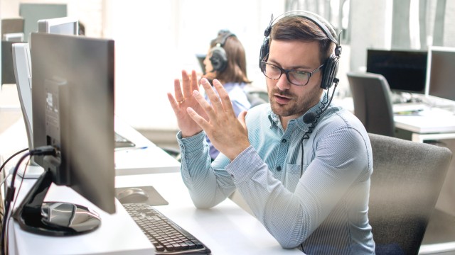Muž se sluchátky na uších vysvětluje něco před svým počítačem